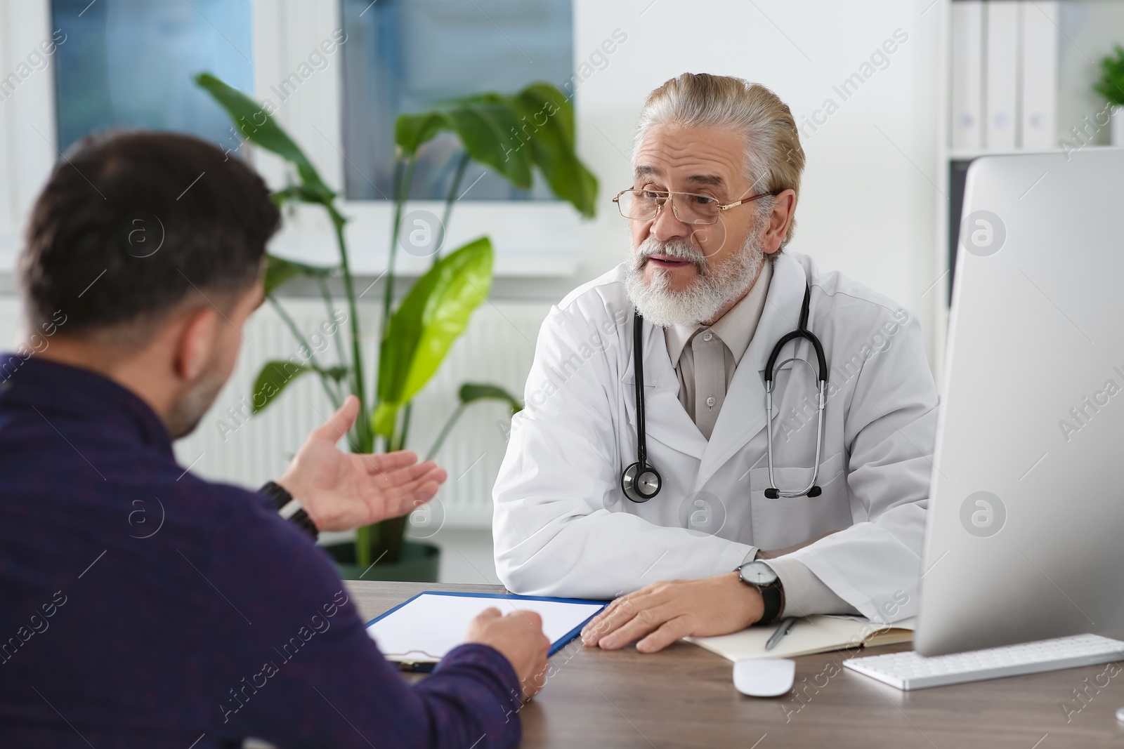 Photo of Senior doctor consulting patient at wooden table in clinic