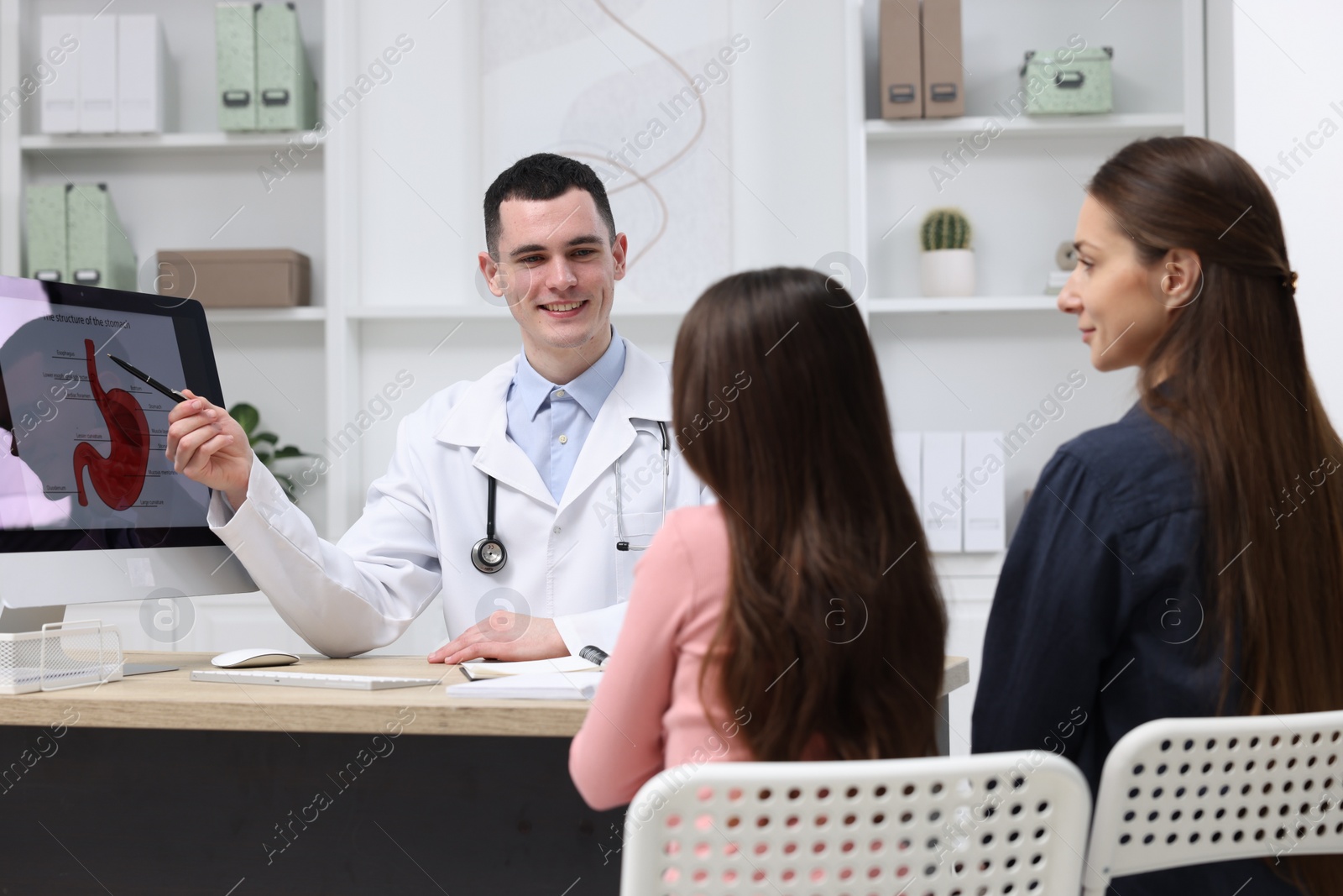 Photo of Gastroenterologist consulting woman with her daughter and showing image of stomach on computer in clinic