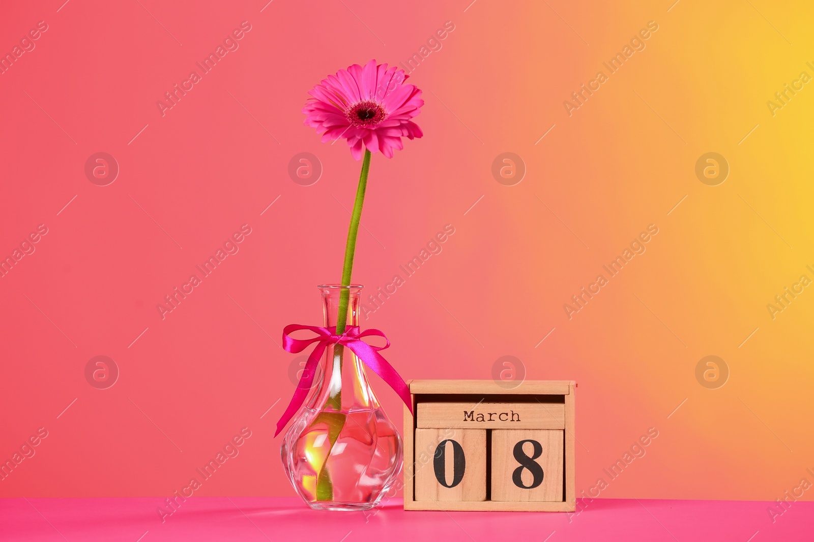 Photo of Vase with beautiful flower and wooden block calendar on table against color background. International Women's Day