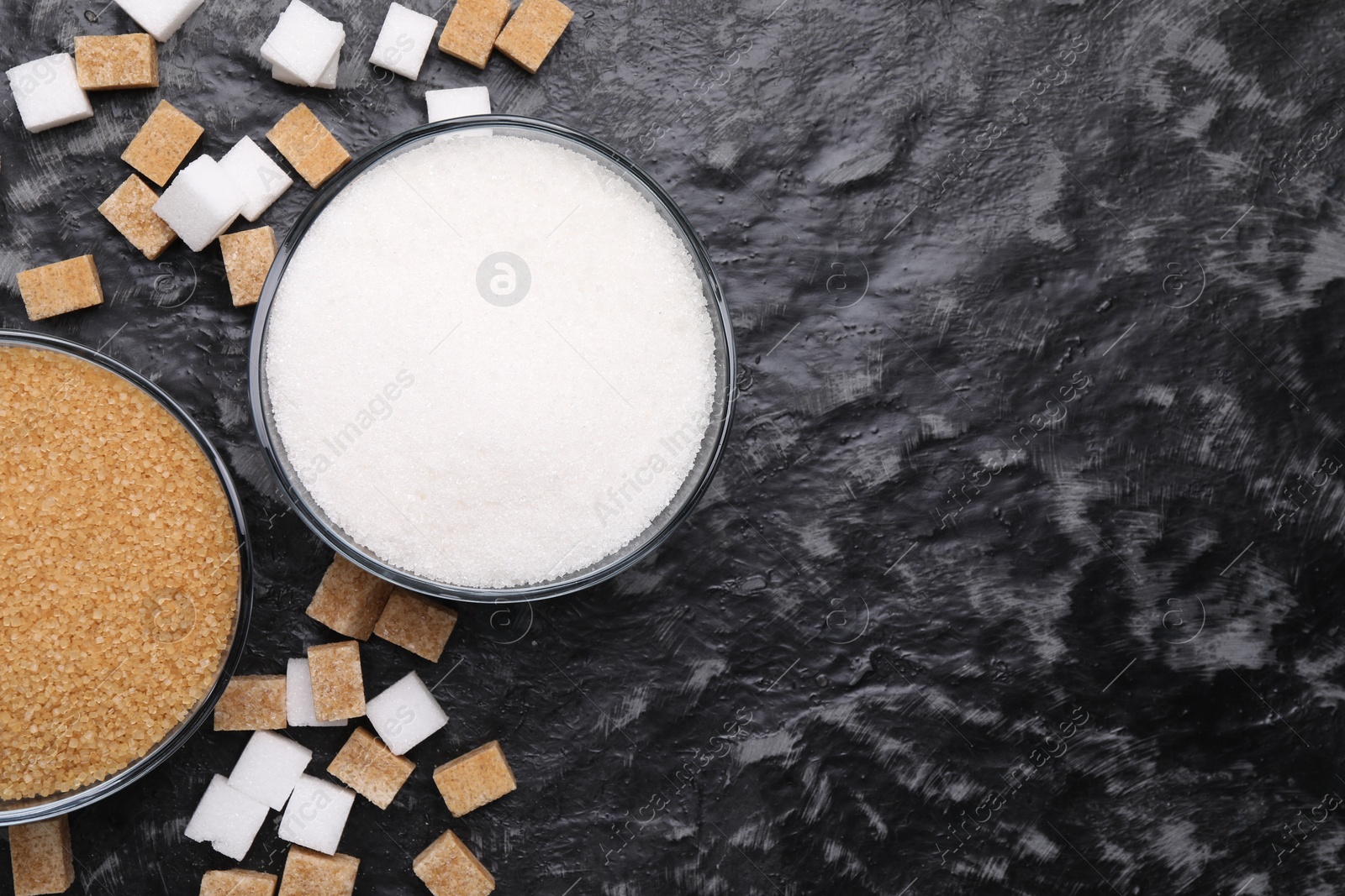 Photo of Different types of sugar in bowls on dark gray textured table, flat lay. Space for text