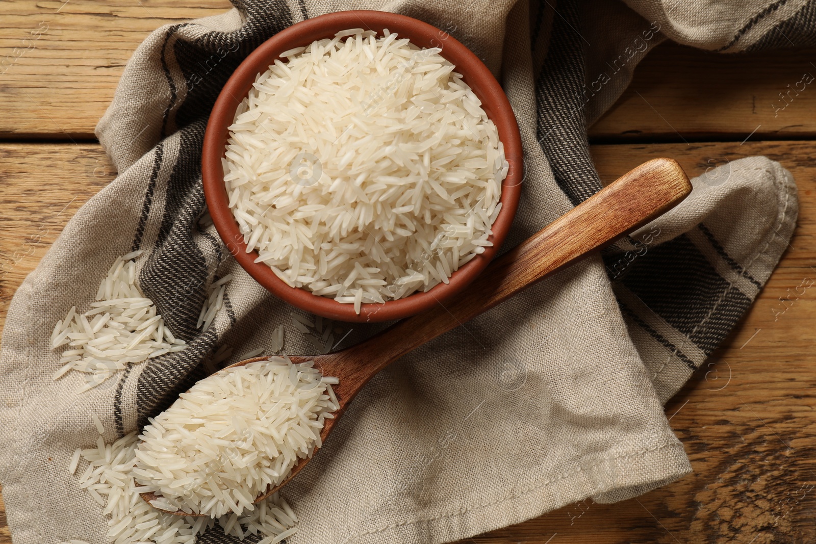 Photo of Raw basmati rice in bowl and spoon on wooden table, top view