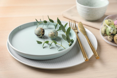 Festive Easter table setting with quail eggs and floral decoration on wooden background