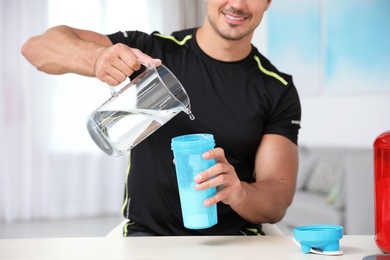Photo of Young athletic man preparing protein shake at home, closeup view