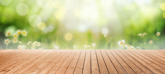 Empty wooden surface and blurred view of beautiful blooming chamomiles in green meadow. Bokeh effect