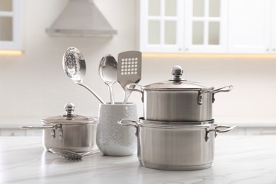 Set of stainless steel cookware and kitchen utensils on white table indoors