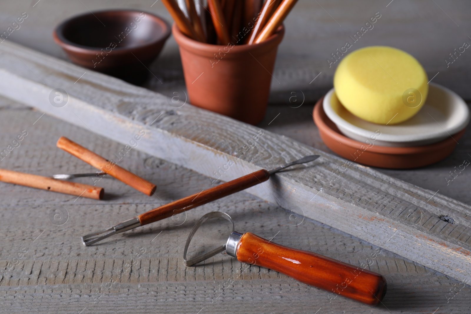 Photo of Set of different crafting tools and clay dishes on grey wooden table, closeup