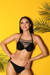 Photo of Beautiful young woman in black bikini and tropical leaves on yellow background