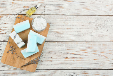 Flat lay composition with natural handmade soap and ingredients on white wooden table, space for text