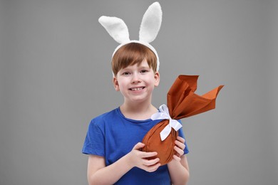 Easter celebration. Cute little boy with bunny ears and wrapped egg on grey background