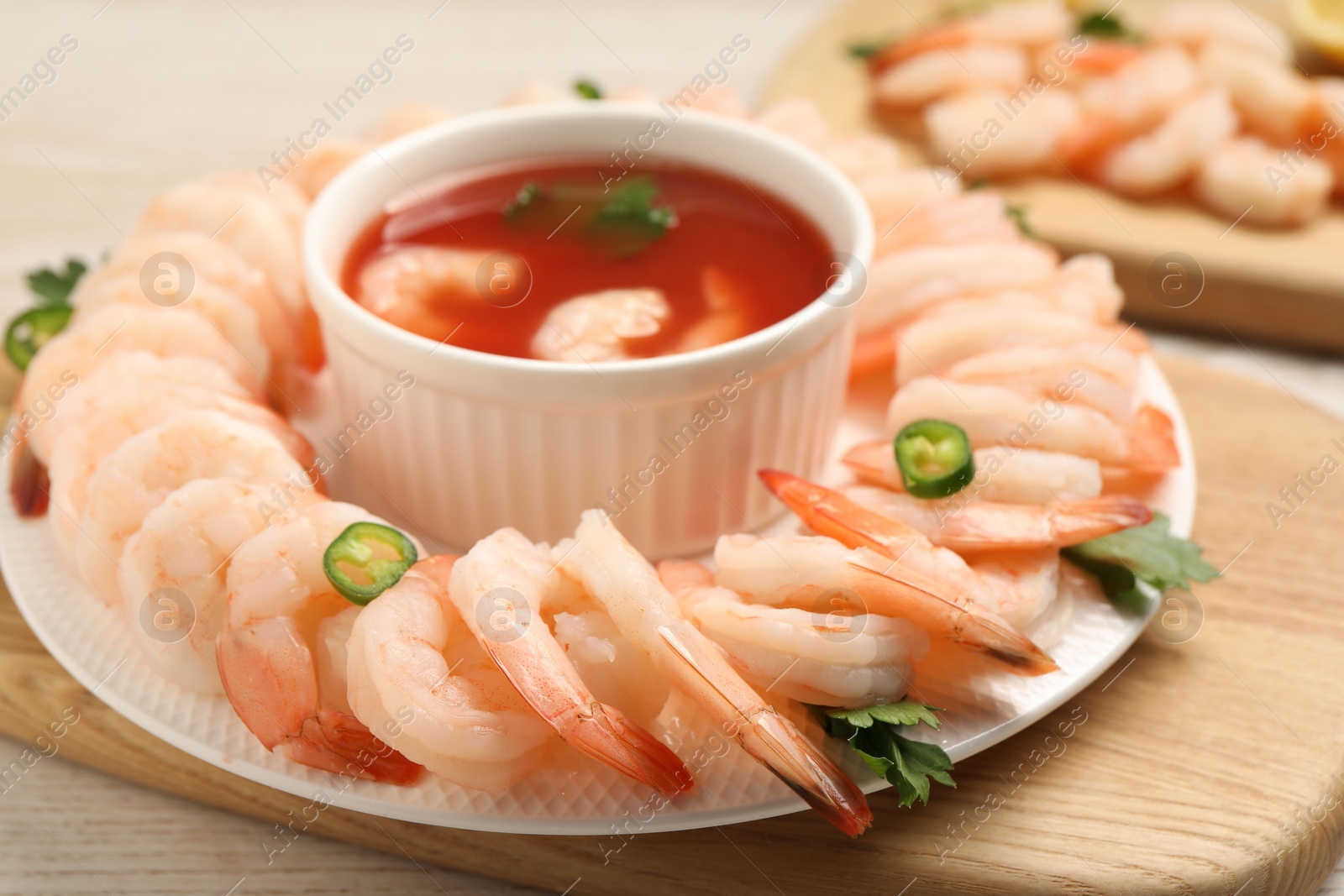 Photo of Tasty boiled shrimps with cocktail sauce, chili and parsley on light wooden table, closeup