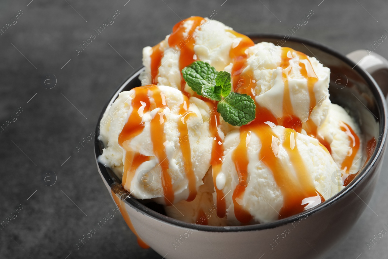 Photo of Tasty ice cream with caramel sauce in mug on table, closeup