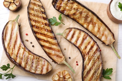 Photo of Delicious grilled eggplant halves and sauce on table, flat lay