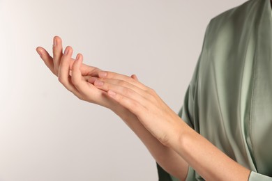 Woman applying cosmetic cream onto hand on light grey background, closeup