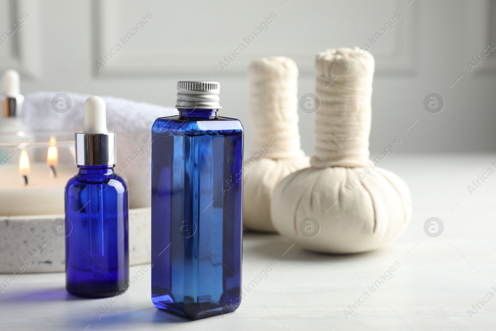 Photo of Spa composition. Bottles of cosmetic products, herbal bags and burning candle on light table