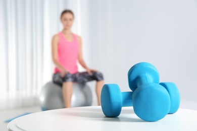 Photo of Dumbbells on table and woman doing fitness exercises at home. Space for text