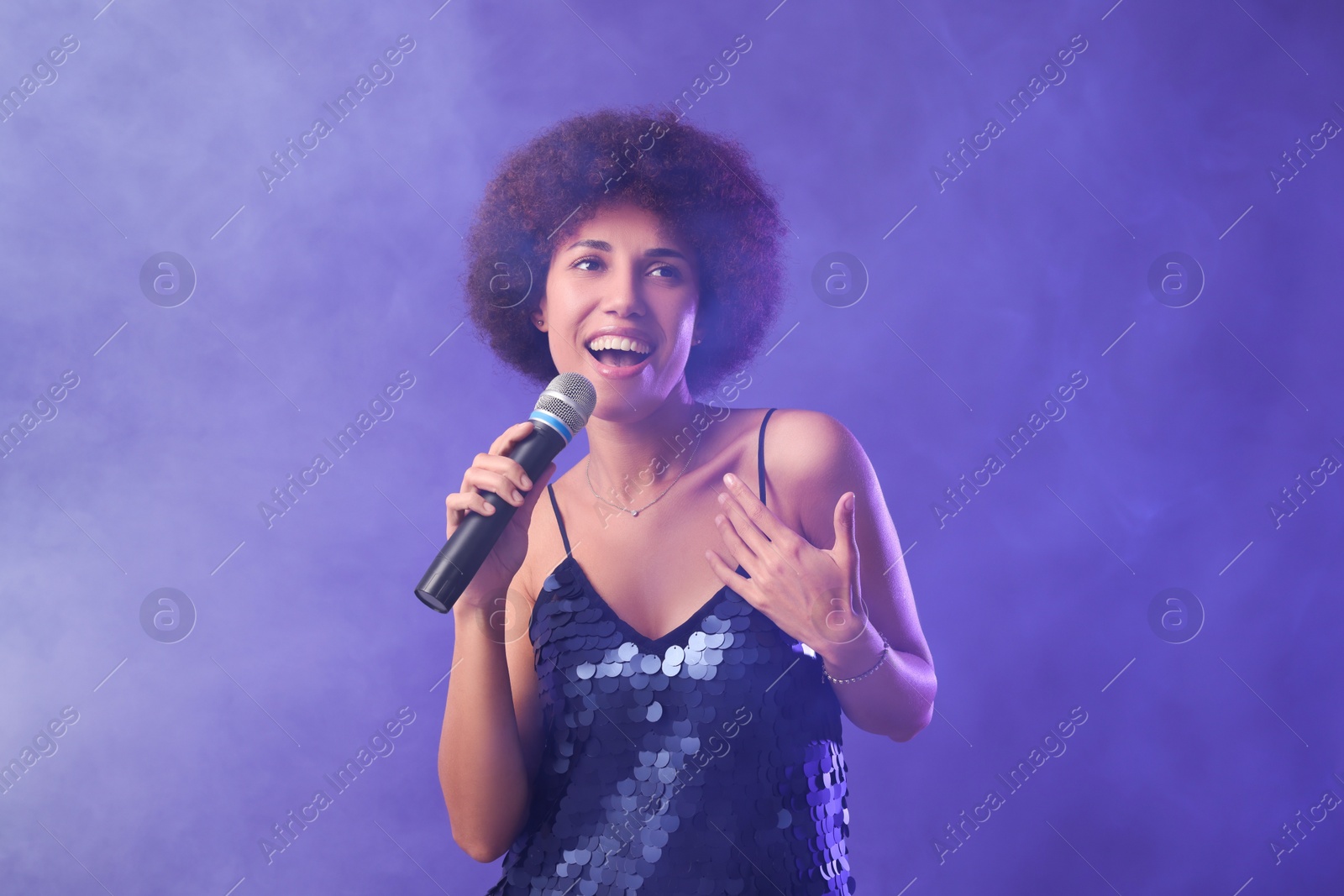 Photo of Curly young woman with microphone singing on purple background