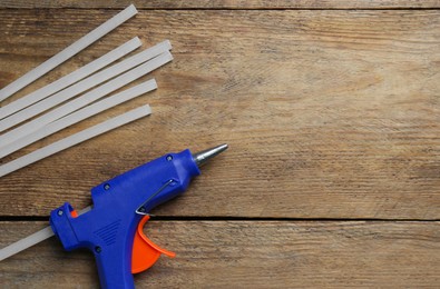 Blue glue gun and sticks on wooden table, flat lay. Space for text