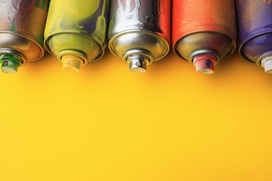 Photo of Used cans of spray paints on yellow background, space for text. Graffiti supplies