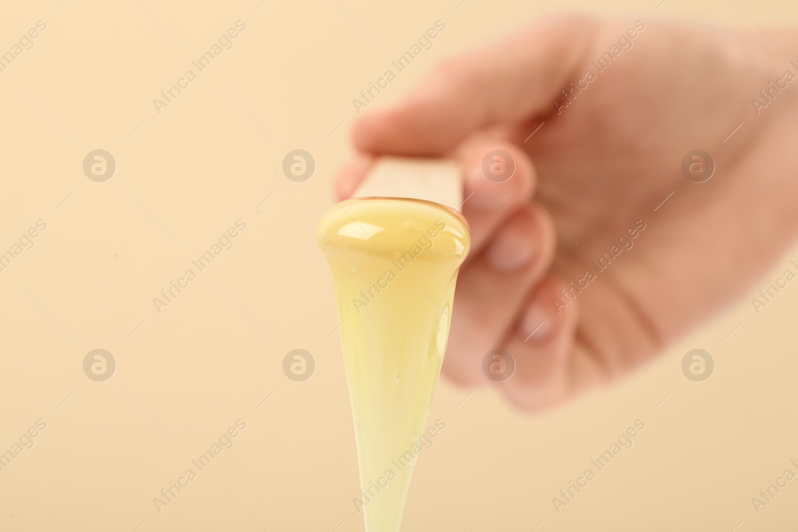 Photo of Woman holding spatula with hot depilatory wax on beige background, closeup