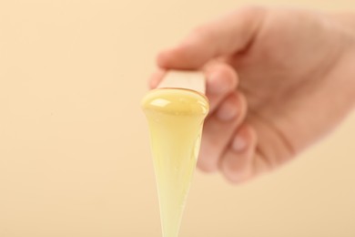 Photo of Woman holding spatula with hot depilatory wax on beige background, closeup