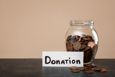 Photo of Donation jar and coins on table against color background. Space for text