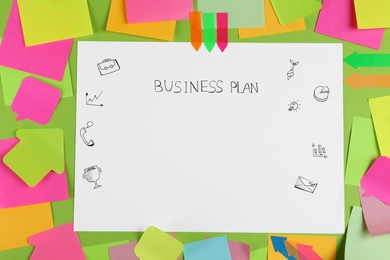 Sheet of paper with words Business Plan and sticky notes on green background, flat lay