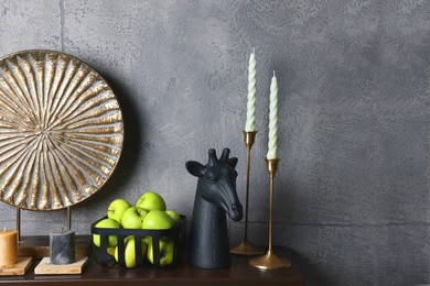Wooden shelf with candles, decorative figure of giraffe, plate and apples against grey wall