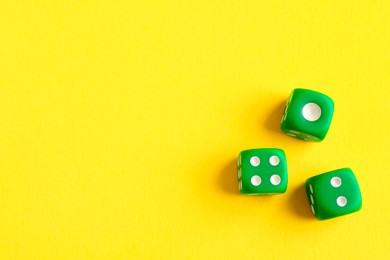 Photo of Three green game dices on yellow background, flat lay. Space for text