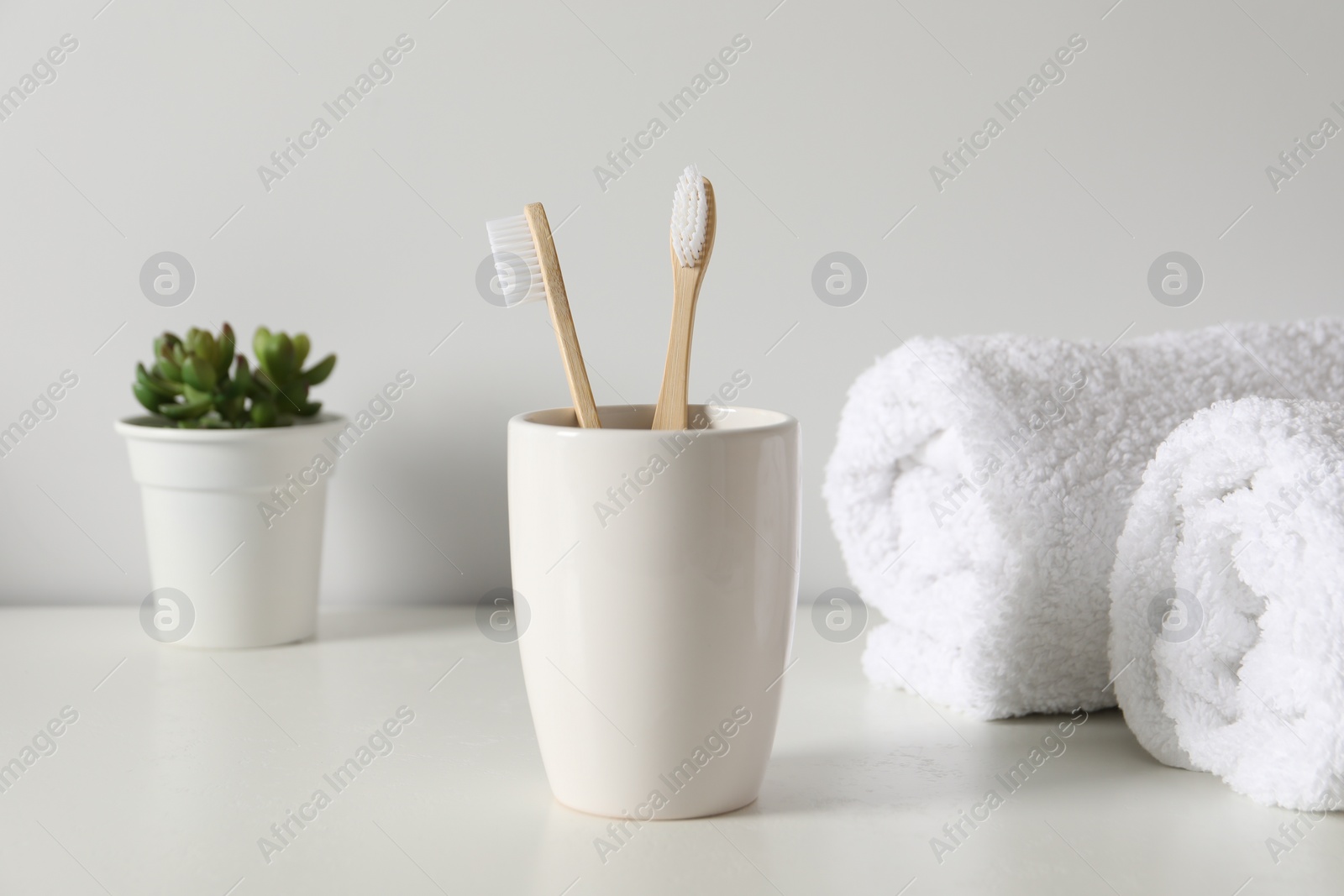Photo of Bamboo toothbrushes in holder, potted plant and towels on white countertop