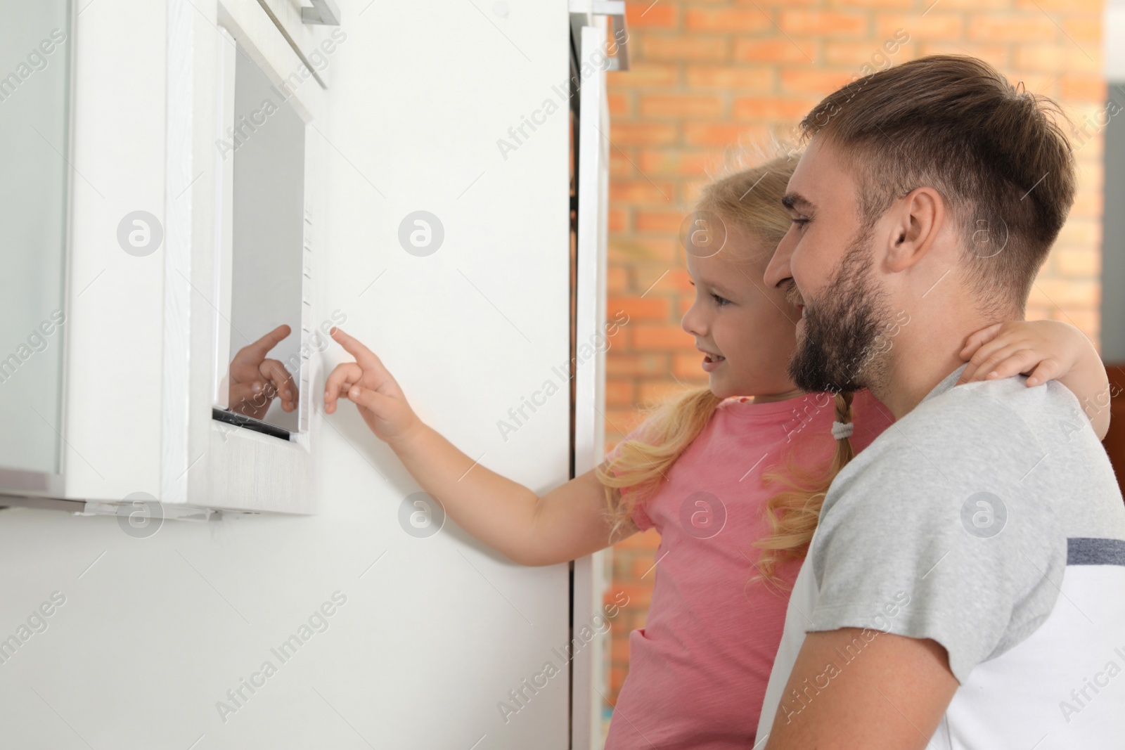 Photo of Little daughter and father using microwave oven in kitchen