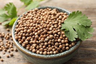 Dried coriander seeds in bowl and green leaves on table, closeup