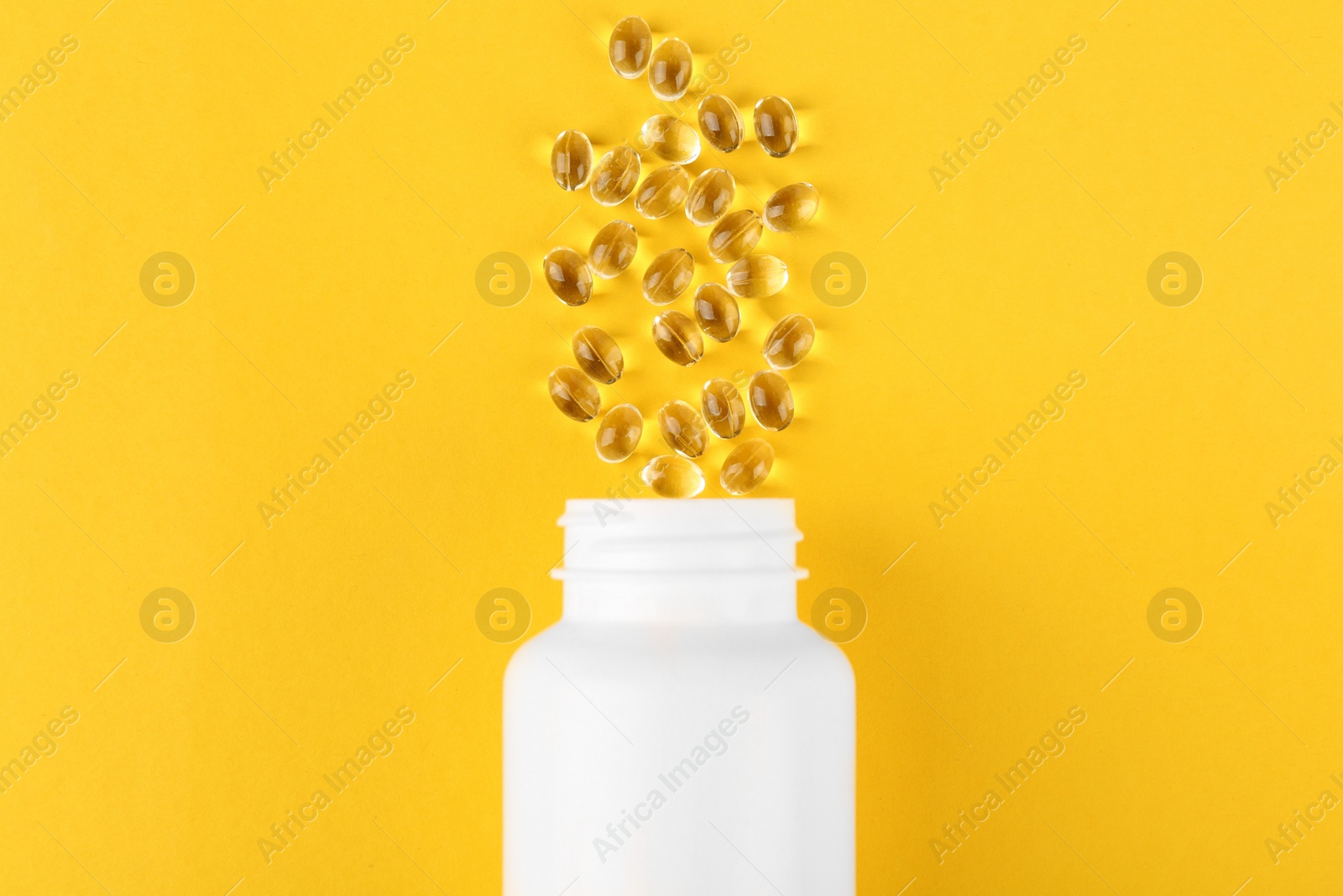 Photo of White medical bottle and vitamin capsules on yellow background, top view