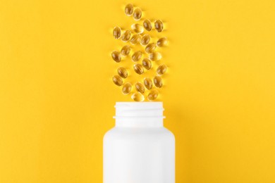 Photo of White medical bottle and vitamin capsules on yellow background, top view