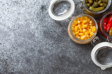 Photo of Flat lay composition with jars of pickled vegetables on grey table. Space for text