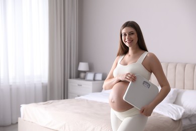 Photo of Young pregnant woman with scales in bedroom. Space for text