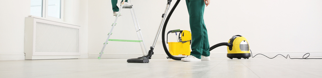 Image of Professional young janitor using vacuum cleaner indoors, closeup view. Banner design