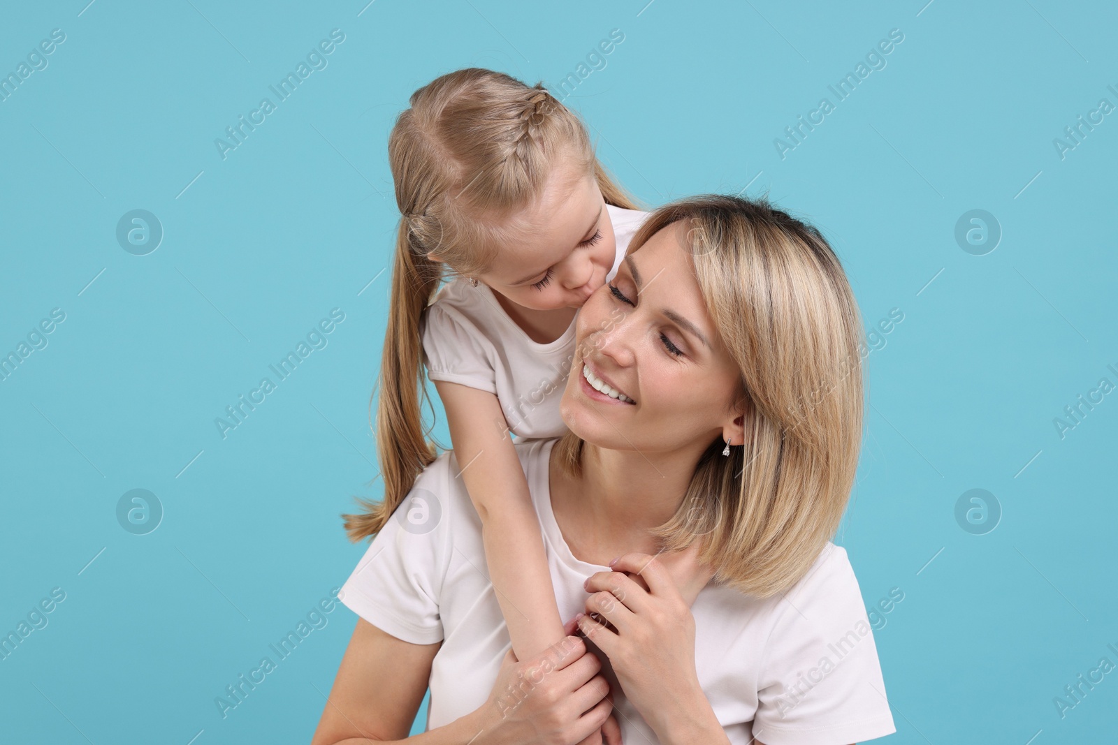 Photo of Daughter kissing her happy mother on light blue background