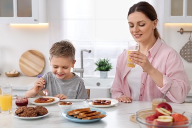 Photo of Mother and her cute little son having breakfast at table in kitchen