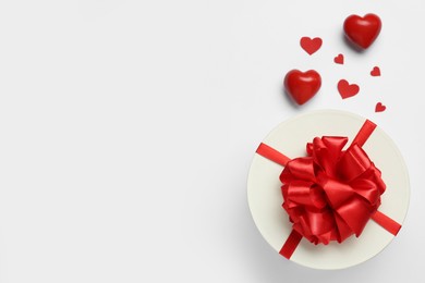 Photo of Gift box with red bow and decorative hearts on white background, top view