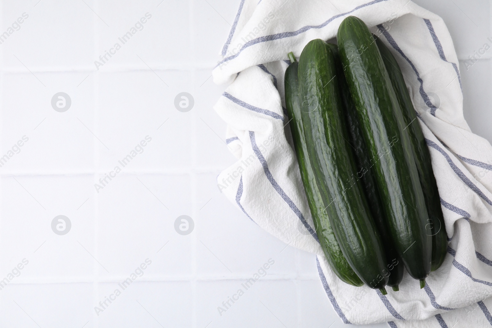 Photo of Fresh cucumbers and cloth on white tiled table, top view. Space for text