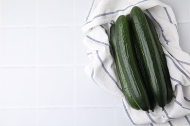 Fresh cucumbers and cloth on white tiled table, top view. Space for text