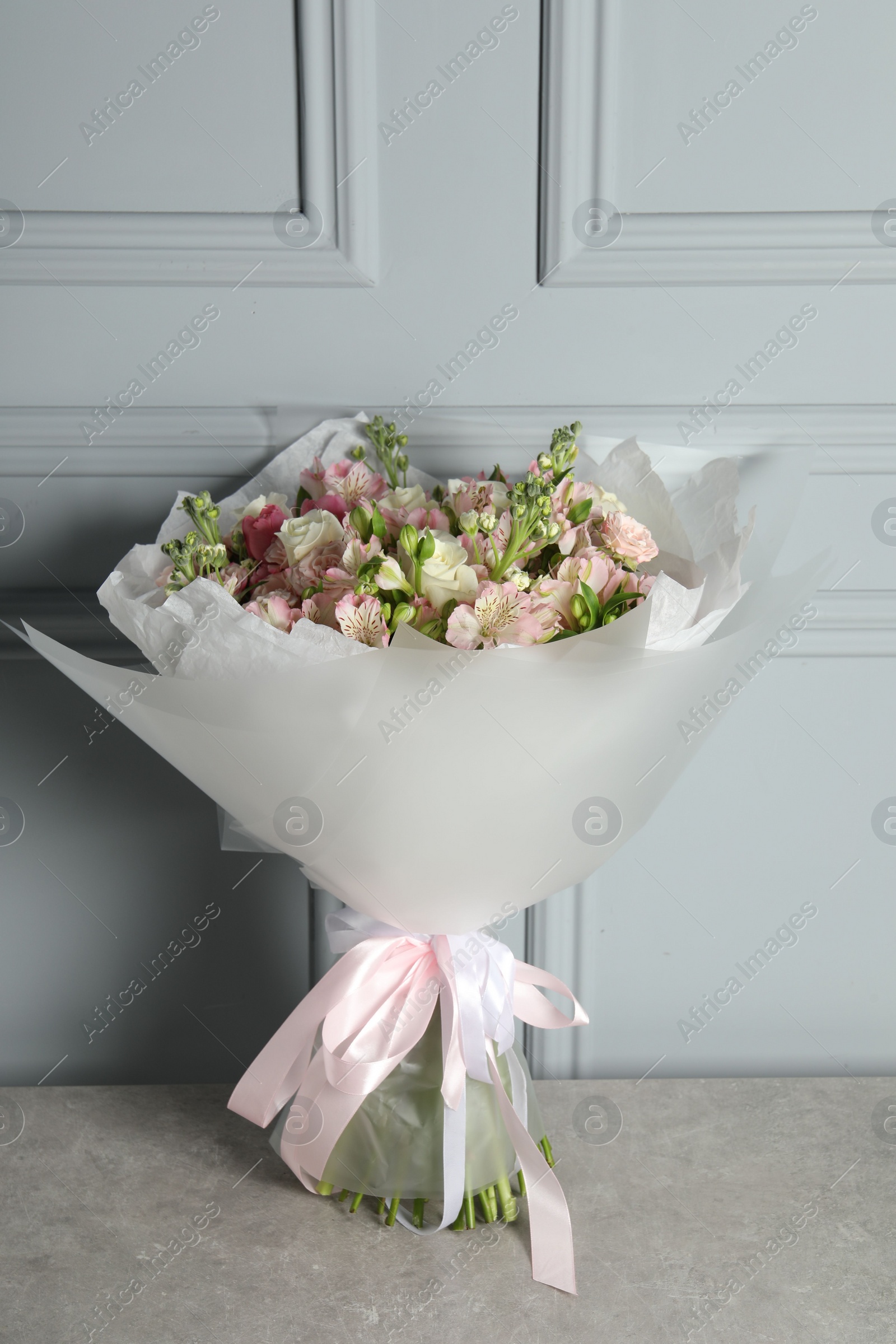 Photo of Beautiful bouquet of fresh flowers on table near grey wall