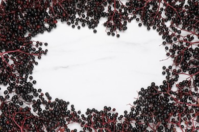 Frame of ripe elderberries on white marble table, flat lay. Space for text