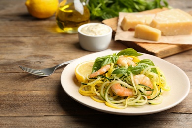 Photo of Delicious zucchini pasta with shrimps, lemon and basil on wooden table