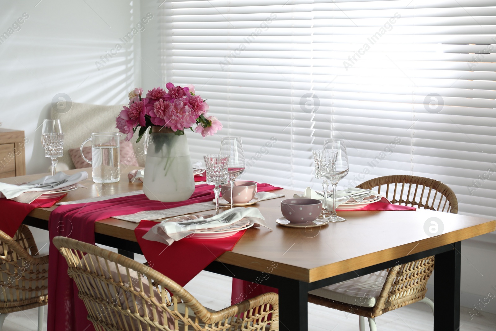 Photo of Pink peonies on table with beautiful setting and rattan chairs in dining room