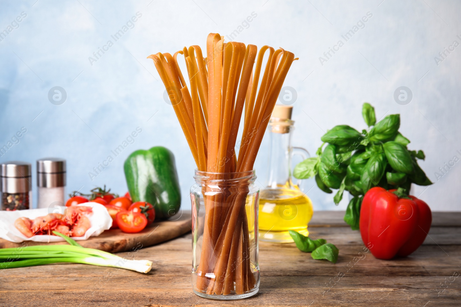 Photo of Jar with uncooked buckwheat noodles and fresh ingredients on wooden table