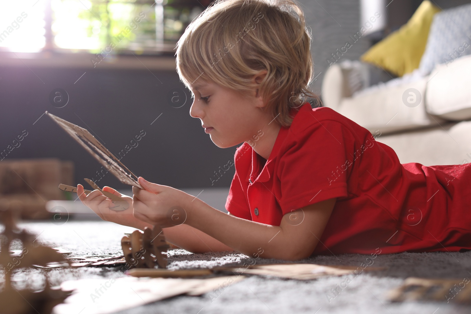 Photo of Little boy making cardboard toys on floor at home. Creative hobby