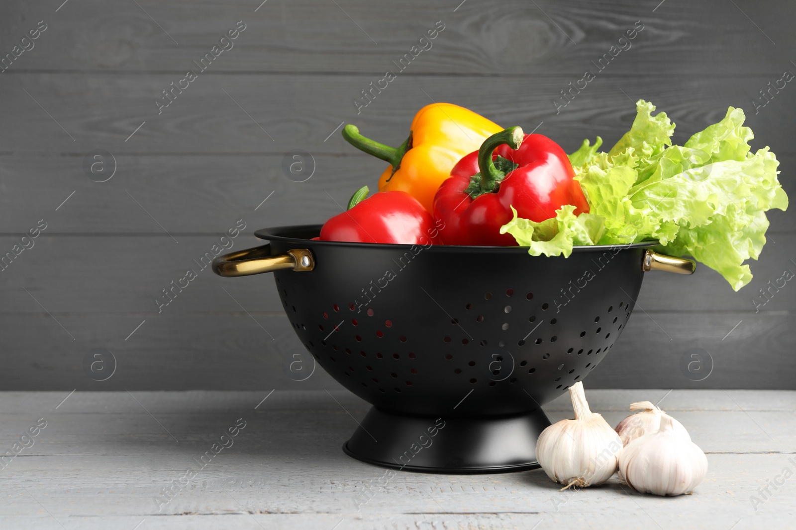 Photo of Black colander and different vegetables on rustic wooden table. Space for text