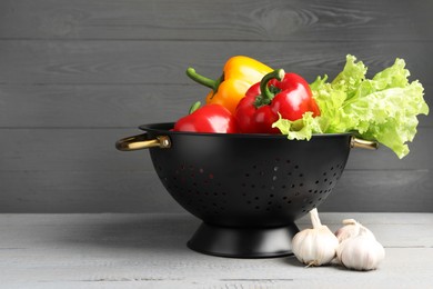 Black colander and different vegetables on rustic wooden table. Space for text