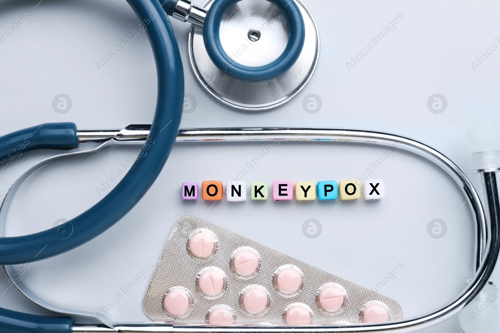Photo of Word Monkeypox made of colorful plastic beads, pills and stethoscope on light background, flat lay